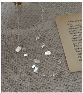 Dettaglio della collana a sfere d'argento con pendenti geometrici su sfondo di libro vintage