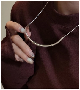 Gros plan du collier minimaliste en tube courbé argenté sur un pull bordeaux