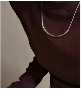 Détail d'un collier en argent S925 avec tube incurvé sur un col roulé foncé