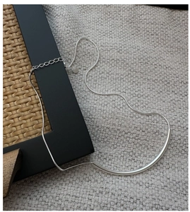 Détail du collier S925 en argent avec tube courbé et chaîne serpent sur texture
