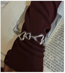 Gros plan du bracelet à maillons cœur en argent S925 sur une manche en tricot rouge foncé