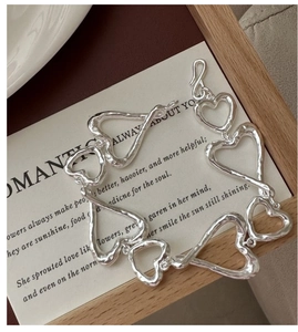 Détail macro du bracelet cœur en argent S925 avec texture martelée sur une carte blanche