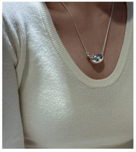 Close-up of minimalist silver bean pendant on white knit sweater showing mirror finish