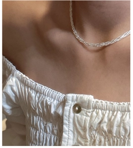 Close-up of elegant woven silver necklace worn by model on a white textured background