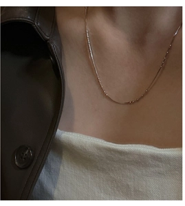 Detail of a gold snake chain necklace with beads on a model wearing a leather jacket