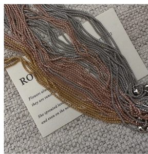 Detail of silver, rose gold and yellow gold beaded chains on textured fabric
