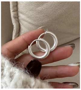 Detailed view of matte brushed silver hoop earrings held against a beige fabric background