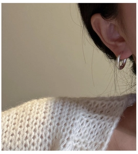 Close-up of a minimalist silver hoop earring worn by a model in a cozy knit sweater