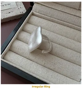 Detail view of a matte silver irregular ring placed in a beige velvet jewelry box