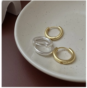 Detail of minimalist matte gold and silver hoop earrings on a ceramic dish