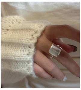 Gros plan d'une bague carrée en argent mat portée avec un pull en maille confortable en fond