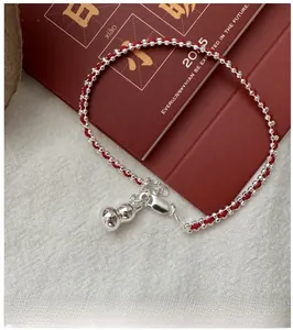 Detail of red braided string bracelet with S925 silver hulu charm on a desk