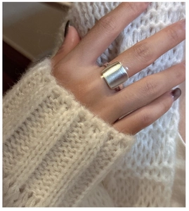 Gros plan d'une bague carrée en argent mat portée sur un pull en maille beige doux