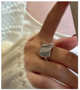Détail d'une bague carrée en argent mat portée au doigt sous une lumière douce