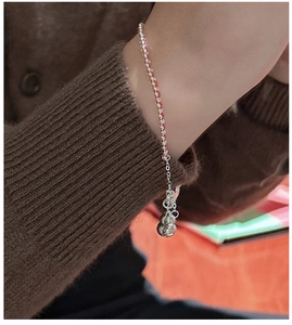 Macro view of woven red cord bracelet with silver gourd charm on a model wrist