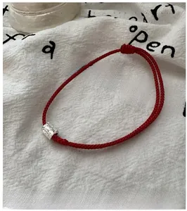 Gros plan du bracelet en corde rouge tressée avec perle en argent martelé sur tissu lin