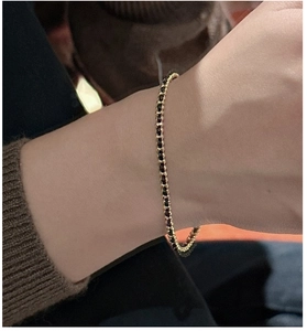 Detail of a thin gold chain bracelet with tiny black beads worn on a wrist over a dark knit sleeve
