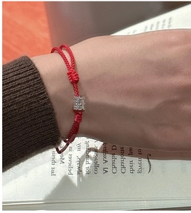 Détail macro du bracelet en cordon rouge tressé avec une perle cylindrique argentée texturée
