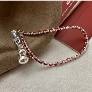 Detail of red braided cord bracelet with silver beads and polished gourd pendant charm