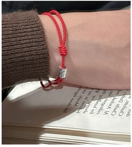 Détail d'un bracelet en corde tressée rouge avec perles argentées martelées au poignet