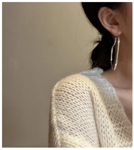 Close-up of a large irregular streamline silver hoop earring worn by a model