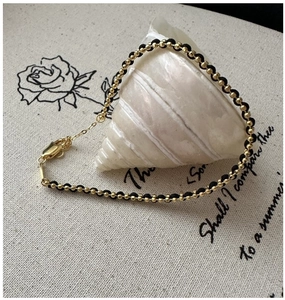 Detail of adjustable black cord bracelet with gold beads over a decorative conch shell
