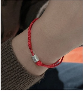 Gros plan du bracelet en corde rouge tressée avec perle argentée martelée au poignet