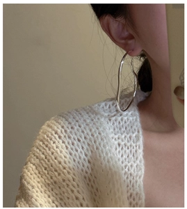 Detailed close-up of large wavy silver hoop earrings on a model showing sleek design