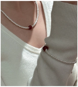Detail of red agate and white bead jewelry set worn on a stylish knit sweater background