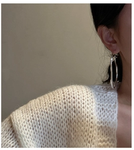 Macro shot of silver oversized hoop earrings with a stylish irregular wavy texture on ears