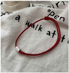 Détail du bracelet en corde rouge avec perle en métal argenté martelé sur lin blanc