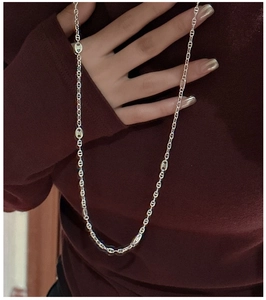 Gros plan d'un collier chaîne à maillons nez de porc argenté sur un pull en maille rouge foncé