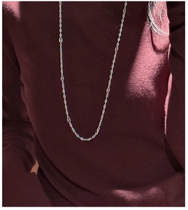 Détail d'un collier chaîne d'ancre argenté porté sur un pull à col roulé rouge