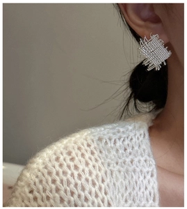 Detailed view of silver woven mesh earrings worn on ear with soft beige sweater