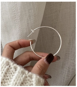 Gros plan d'une grande créole en argent sterling 925 tenue à la main sur une maille douce