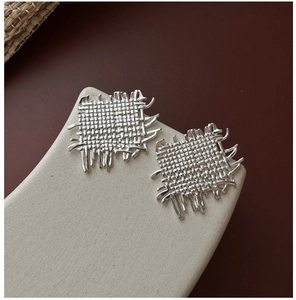 Macro shot of silver woven square earrings with organic fringes on stone display