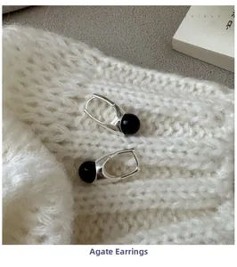 Macro detail of S925 silver black agate earrings on a white knitted sweater background