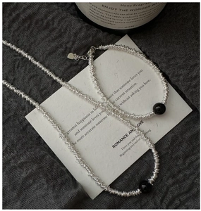 Détail du collier en argent S925 avec perles d'agate noire sur tissu gris texturé