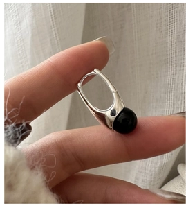 Detail of silver earring with black agate bead held against soft fabric background