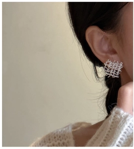 Détail de boucles d'oreilles tissées géométriques en argent portées pour un style minimaliste