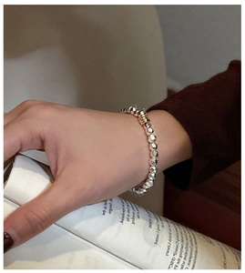 Detail of faceted silver and gold mixed beads on an elastic bracelet worn by a model