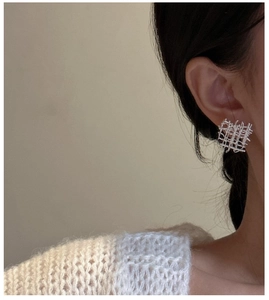 Gros plan de boucles d'oreilles carrées en argent portées sur l'oreille avec tricot doux