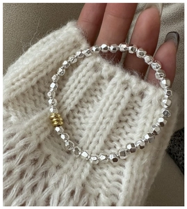 Detail of S925 silver beaded bracelet with gold accents on model wearing a knit sweater
