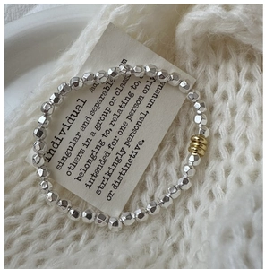 Detailed macro view of S925 silver faceted beads with gold ring accents on a white knit background