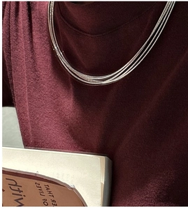 Detailed view of triple-layered S925 sterling silver necklaces on a red knit sweater