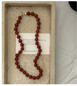 Detailed view of red agate beaded necklace with silver lobster clasp on stone tray