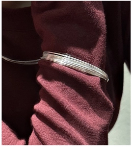 Macro detail of multi-layered S925 sterling silver bangles over dark burgundy sleeve