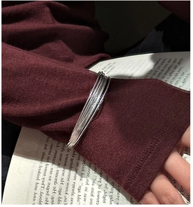 Detailed view of layered S925 sterling silver bracelets over a red knit sleeve and book