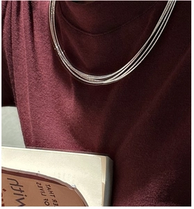 Close-up of triple-layered S925 sterling silver necklaces on a burgundy sweater