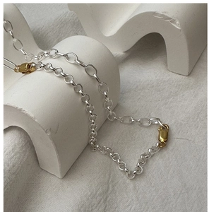 Detail of silver chain necklace with two gold lobster clasps on white geometric props